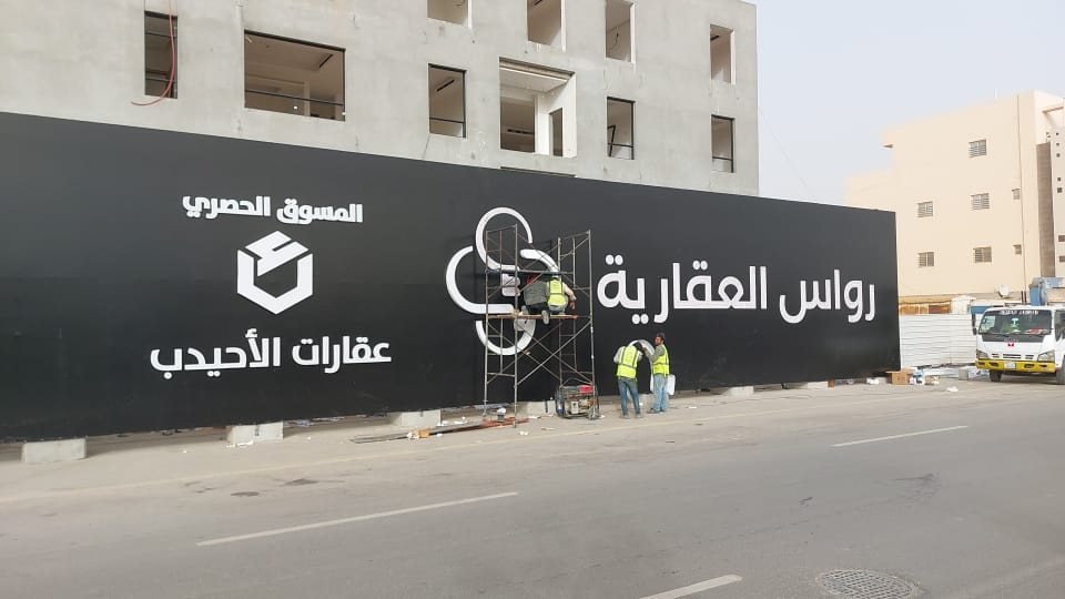 فنيون يركّبون شعارًا مجسّمًا على ساتر موقع