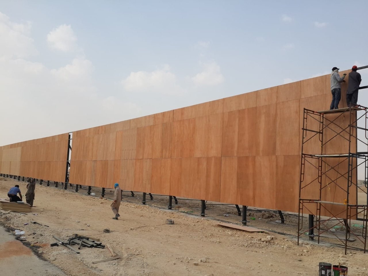 عمال يركّبون ألواح ساتر طويل على هيكل معدني